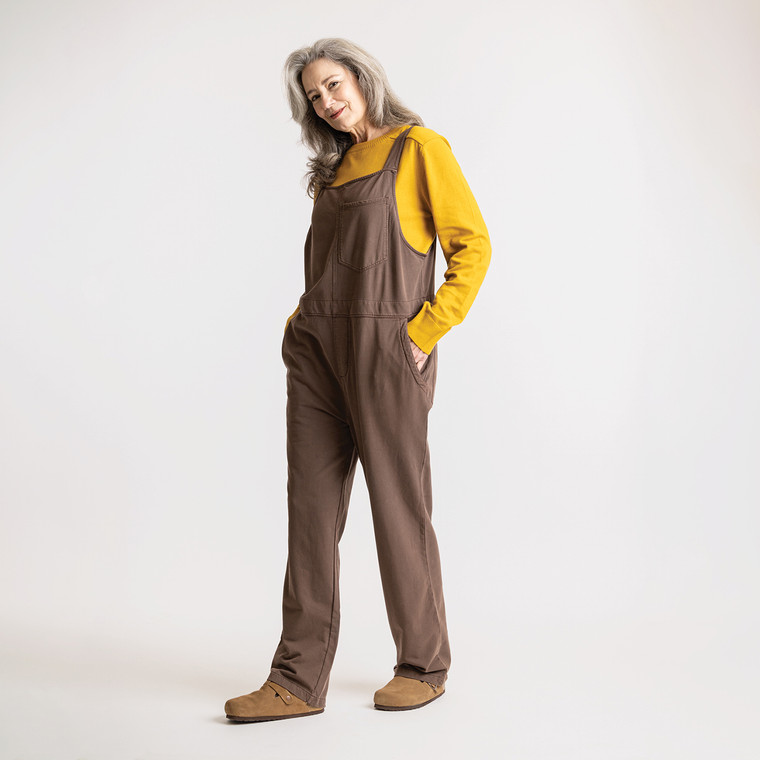 Full body side view of model wearing organic cotton overalls in color chocolate.